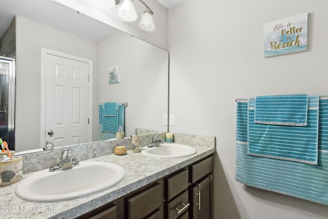 bathroom featuring double vanity, a shower with door, and a sink