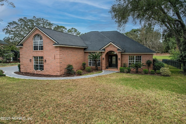 traditional home featuring brick siding, roof with shingles, a front lawn, and fence