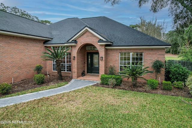 traditional home featuring brick siding, a front lawn, and a shingled roof