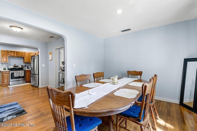 dining room with visible vents, arched walkways, light wood-style floors, and baseboards