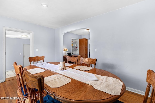 dining space featuring baseboards, arched walkways, and light wood-style floors