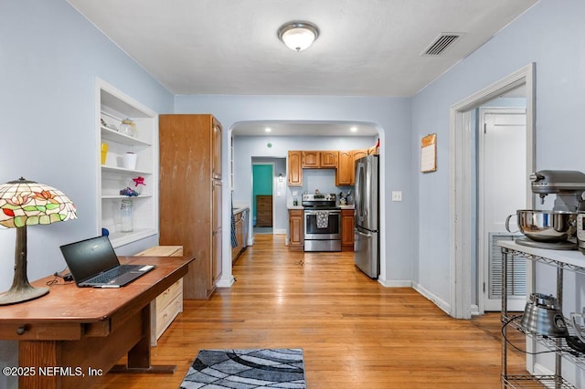 interior space with light wood finished floors, visible vents, brown cabinetry, arched walkways, and stainless steel appliances