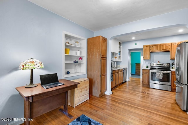 kitchen with light countertops, light wood-type flooring, appliances with stainless steel finishes, arched walkways, and a sink