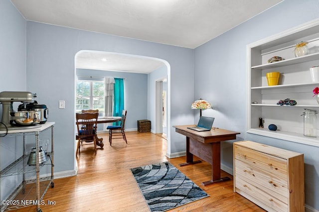 office area featuring baseboards, arched walkways, and light wood-style floors