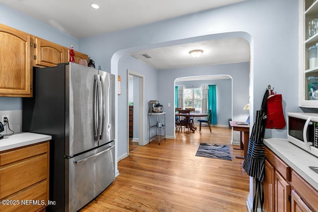 kitchen with arched walkways, light wood-type flooring, light countertops, and freestanding refrigerator