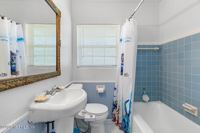 bathroom with a sink, shower / bathtub combination with curtain, toilet, and wainscoting