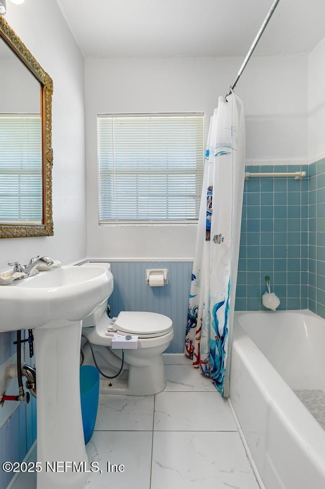 bathroom with a wealth of natural light, a wainscoted wall, toilet, and marble finish floor