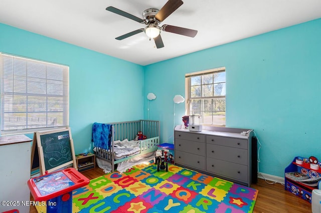 bedroom featuring baseboards, a crib, wood finished floors, and a ceiling fan