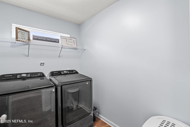 laundry room with laundry area, baseboards, wood finished floors, a textured ceiling, and washing machine and dryer