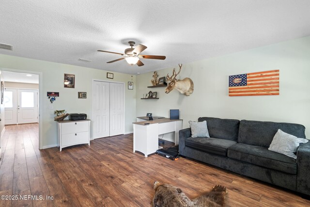 living area featuring a textured ceiling, ceiling fan, dark wood-type flooring, visible vents, and baseboards