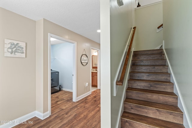 stairs with baseboards, washer / clothes dryer, wood finished floors, a wood stove, and a textured ceiling