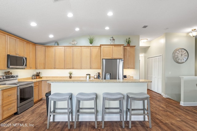 kitchen featuring light brown cabinetry, a kitchen island, stainless steel appliances, and a kitchen breakfast bar