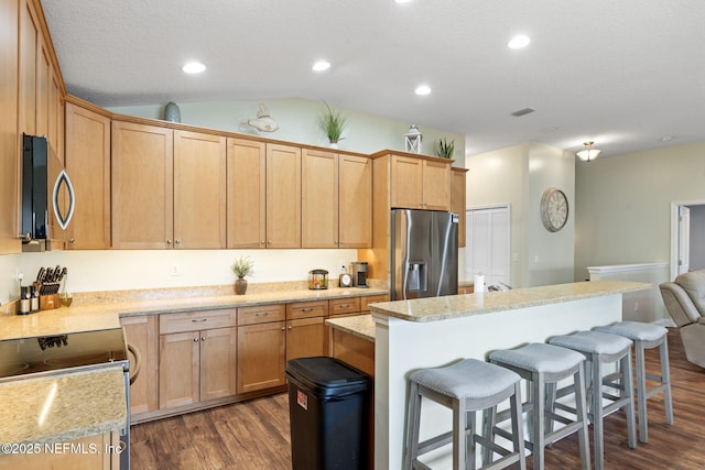 kitchen featuring stainless steel appliances, vaulted ceiling, light countertops, a kitchen bar, and dark wood finished floors