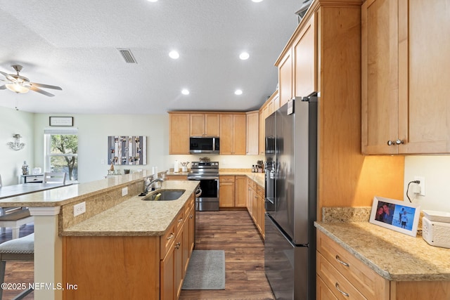 kitchen featuring dark wood-style floors, stainless steel appliances, visible vents, a sink, and a kitchen bar