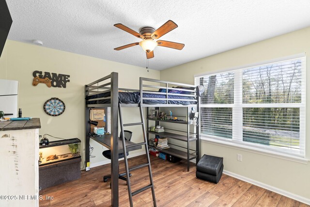 bedroom featuring ceiling fan, a textured ceiling, baseboards, and wood finished floors