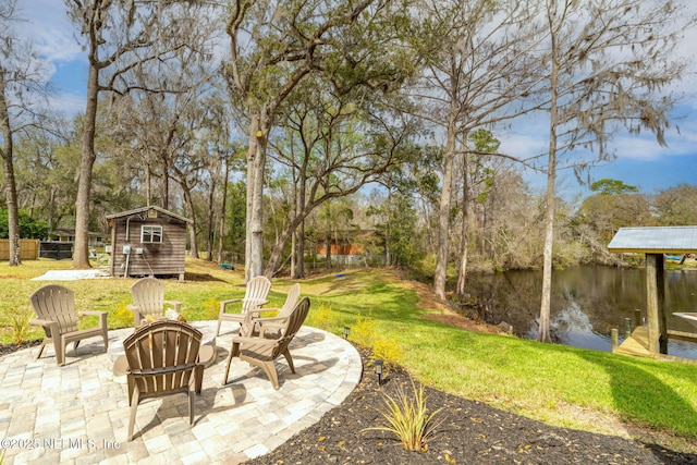 view of yard with an outbuilding, a fire pit, a water view, a shed, and a patio area