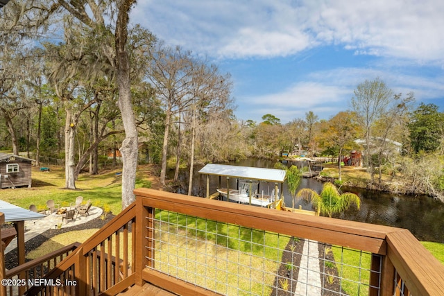 wooden terrace with an outdoor fire pit, a water view, a lawn, and an outbuilding