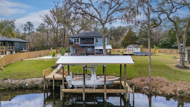 view of dock with boat lift, a fenced backyard, stairway, a deck with water view, and a yard