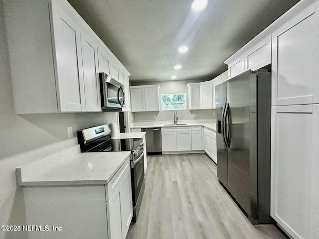 kitchen with stainless steel appliances, light countertops, white cabinets, a sink, and light wood-type flooring