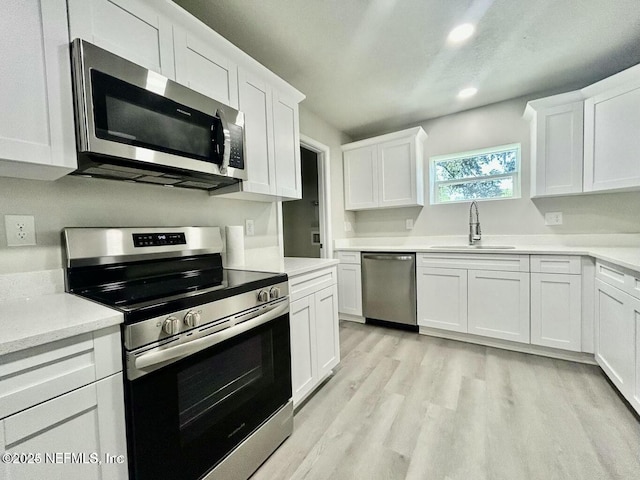 kitchen with light wood finished floors, white cabinets, appliances with stainless steel finishes, light countertops, and a sink