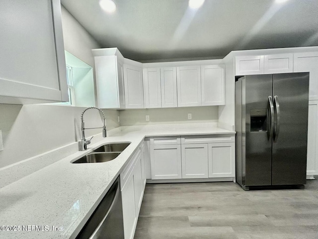 kitchen with white cabinets, light stone countertops, stainless steel appliances, light wood-type flooring, and a sink