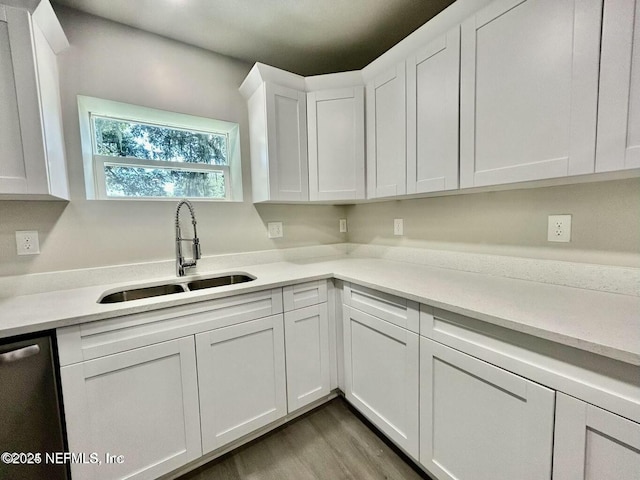 kitchen with wood finished floors, a sink, white cabinets, light countertops, and stainless steel dishwasher