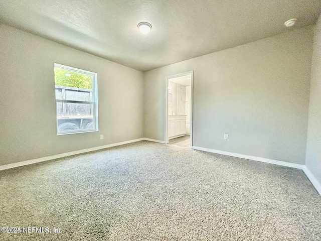 spare room with a textured ceiling, carpet, and baseboards