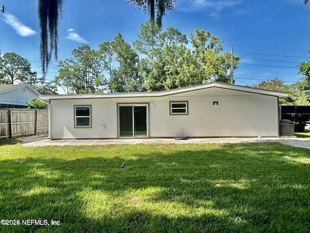 rear view of house with stucco siding, fence, a patio, and a lawn