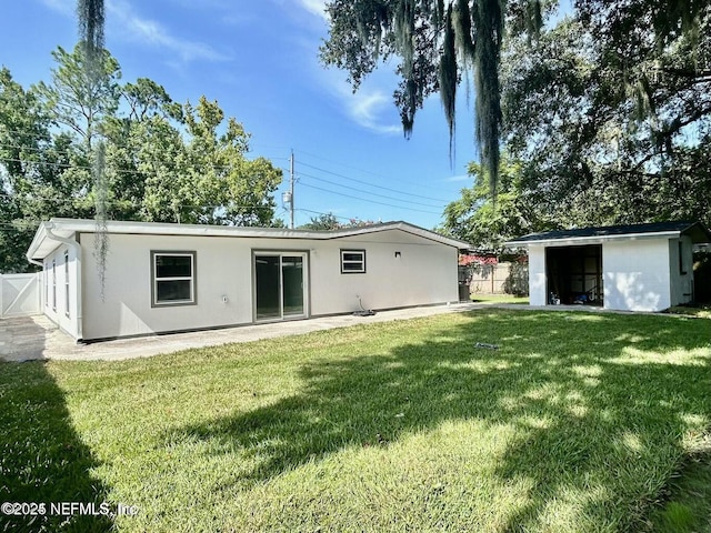 back of property with stucco siding, fence, an outdoor structure, and a lawn