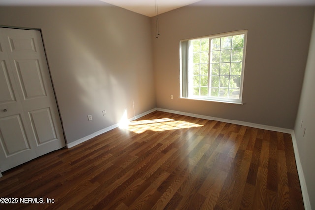 unfurnished room featuring vaulted ceiling, dark wood finished floors, and baseboards