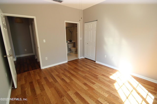 unfurnished bedroom featuring connected bathroom, baseboards, and wood finished floors