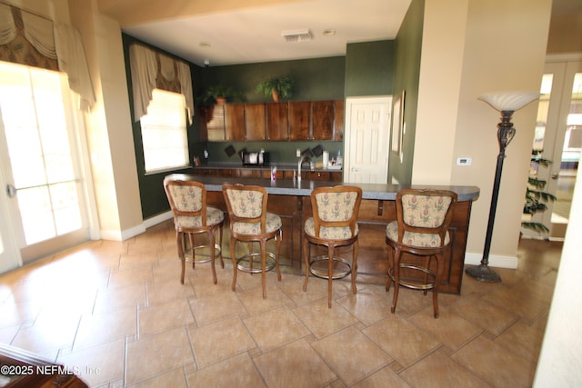 kitchen featuring a breakfast bar area, dark countertops, visible vents, brown cabinetry, and baseboards