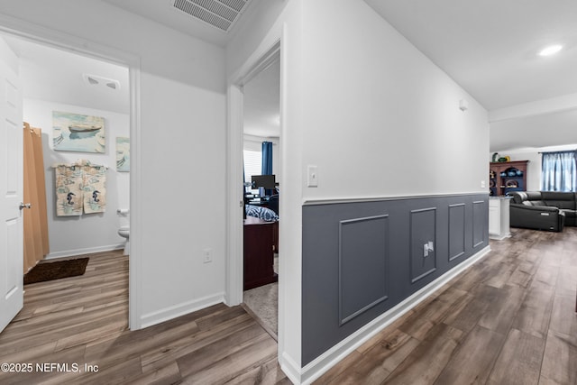 corridor with a wainscoted wall, a decorative wall, wood finished floors, and visible vents