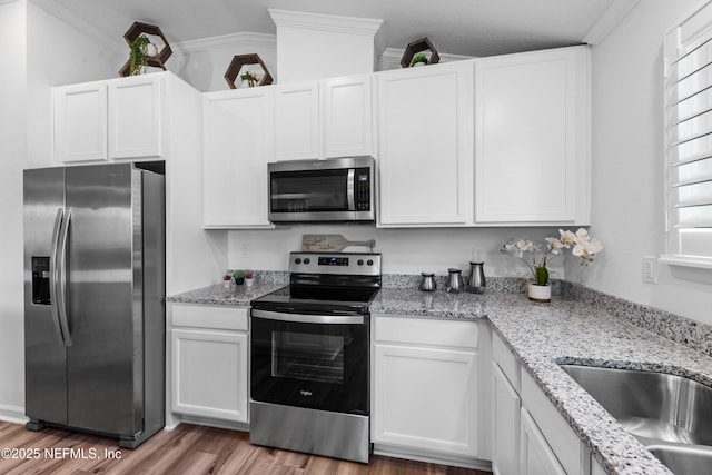 kitchen with crown molding, stainless steel appliances, wood finished floors, white cabinetry, and a sink