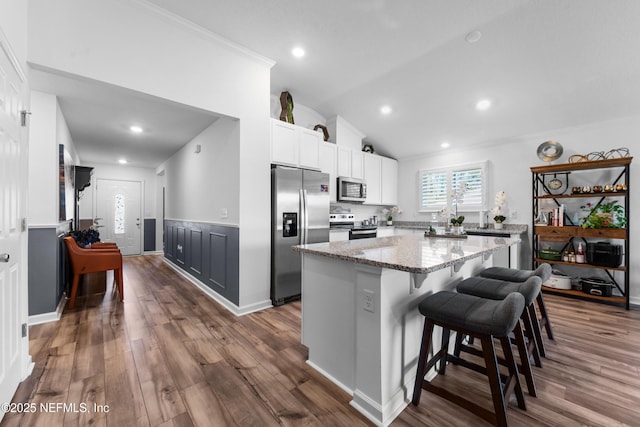 kitchen featuring light stone countertops, dark wood-type flooring, appliances with stainless steel finishes, white cabinetry, and a center island