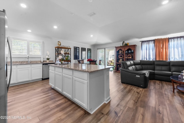 kitchen featuring light wood-style flooring, light stone counters, a center island, white cabinetry, and stainless steel appliances