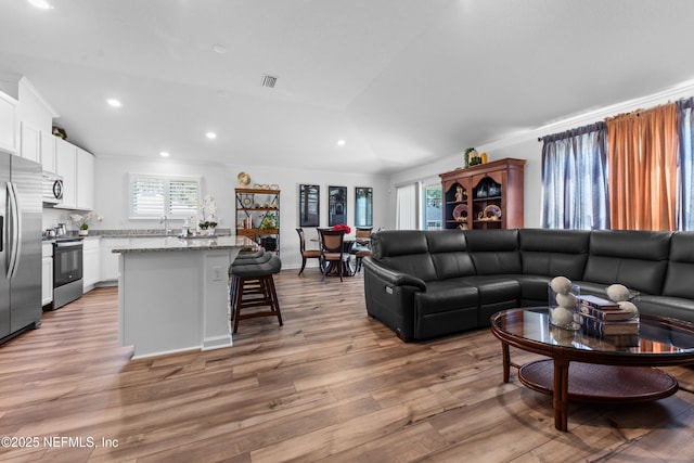 living room with a wealth of natural light, visible vents, lofted ceiling, and light wood-style flooring