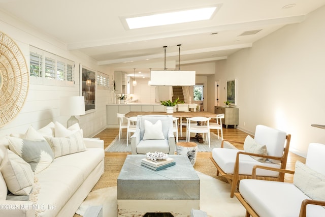 living area featuring lofted ceiling with beams, baseboards, visible vents, and light wood-style floors