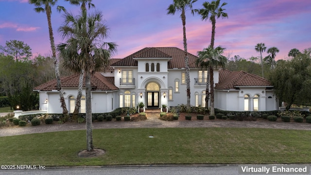 mediterranean / spanish-style home with a front lawn, a tiled roof, french doors, and stucco siding