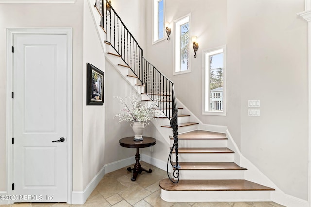 staircase featuring stone tile floors, a high ceiling, and baseboards