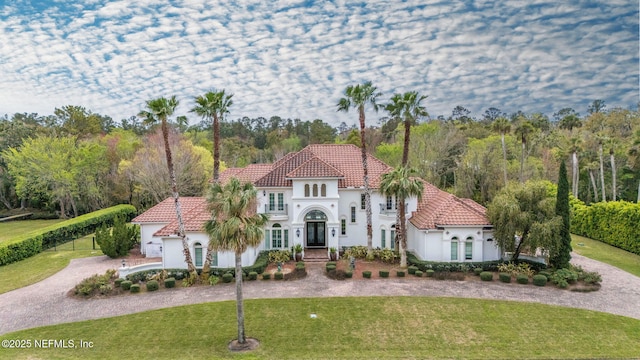 mediterranean / spanish-style house with a front yard, stucco siding, a tile roof, and curved driveway