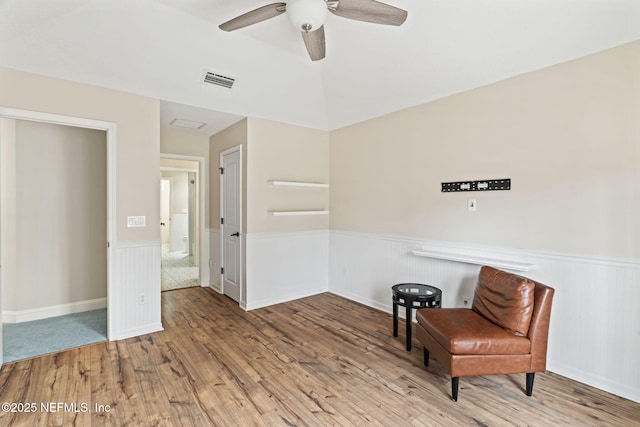 sitting room featuring a wainscoted wall, visible vents, ceiling fan, and wood finished floors