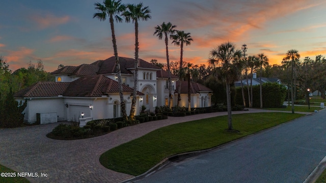 mediterranean / spanish home with curved driveway, a tile roof, stucco siding, a garage, and a yard