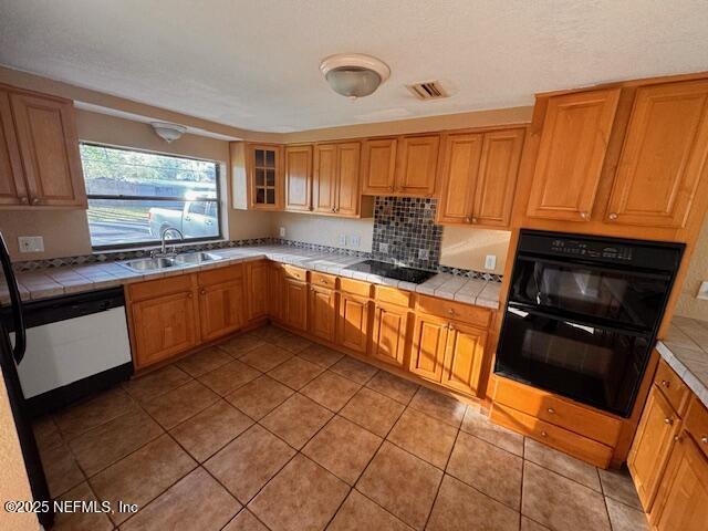 kitchen featuring tile countertops, black appliances, light tile patterned floors, and a sink