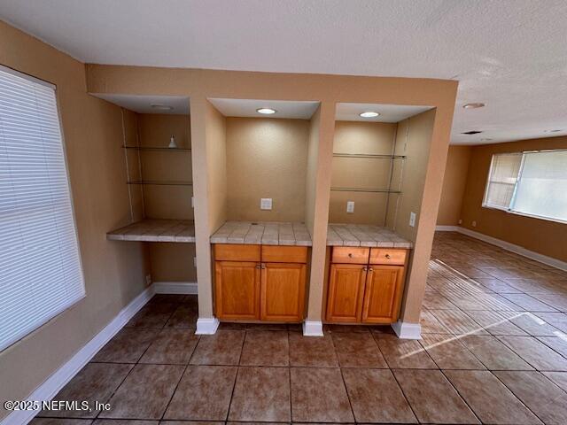 kitchen featuring tile countertops, brown cabinetry, a textured ceiling, dark tile patterned floors, and baseboards