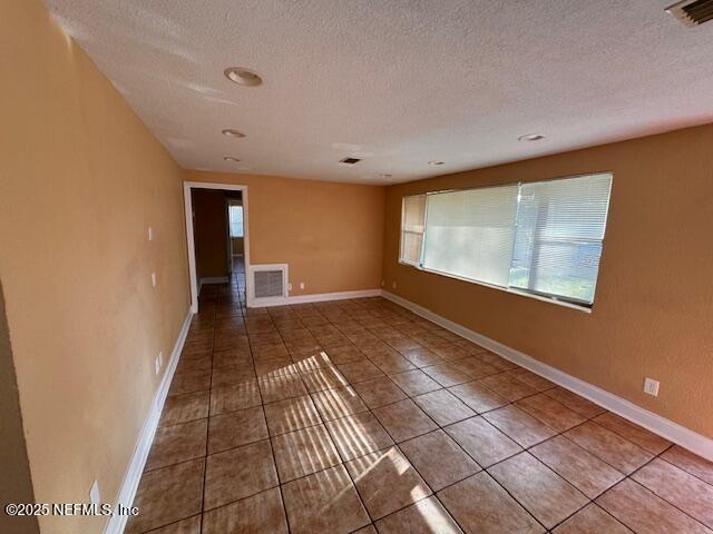 tiled spare room with baseboards, visible vents, and a textured ceiling