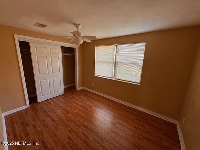 unfurnished bedroom featuring a closet, wood finished floors, visible vents, and baseboards