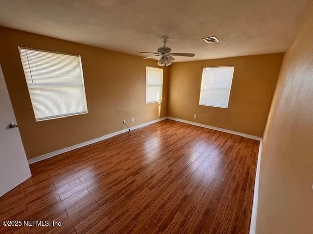 spare room featuring a ceiling fan, visible vents, baseboards, and wood finished floors