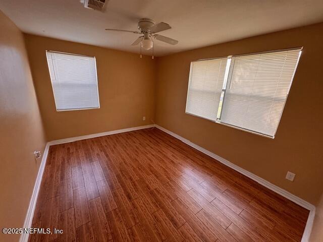 spare room featuring visible vents, a healthy amount of sunlight, ceiling fan, wood finished floors, and baseboards