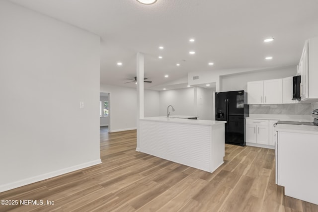 kitchen featuring black appliances, a center island with sink, light countertops, and light wood finished floors